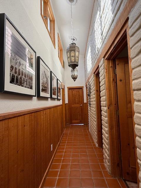 hall featuring dark tile patterned floors, a notable chandelier, and wooden walls