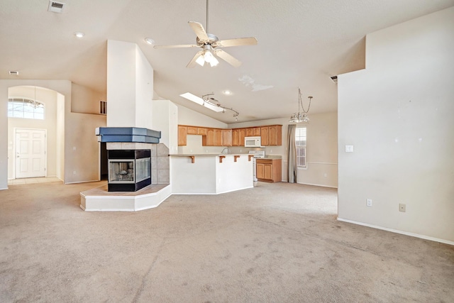 unfurnished living room featuring high vaulted ceiling, ceiling fan, light carpet, and a tiled fireplace