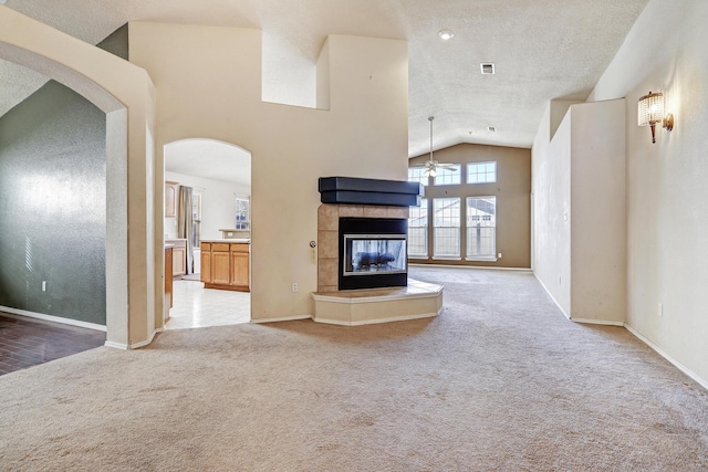 unfurnished living room with light carpet, a tiled fireplace, a textured ceiling, and high vaulted ceiling