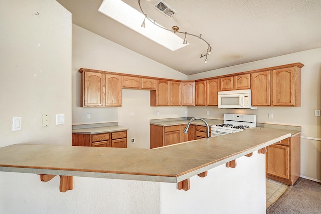 kitchen featuring vaulted ceiling with skylight, white appliances, sink, and a breakfast bar area