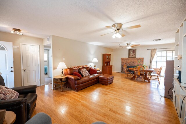 809 Kingman Ave, Grants, NM 87020 - living room featuring visible vents, a fireplace, light wood-type flooring, a ceiling fan, and a textured ceiling