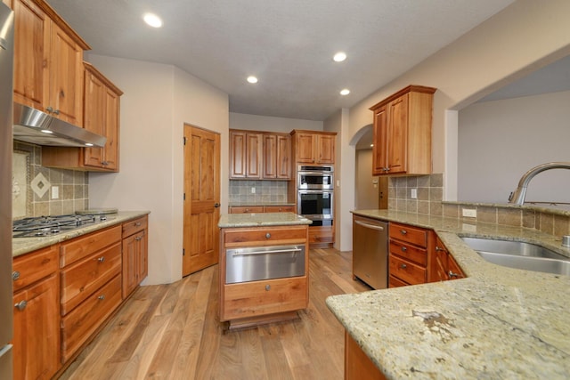 kitchen featuring sink, appliances with stainless steel finishes, light stone counters, tasteful backsplash, and light wood-type flooring