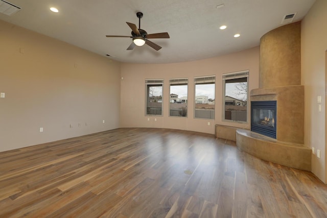 unfurnished living room with a tile fireplace, wood-type flooring, and ceiling fan