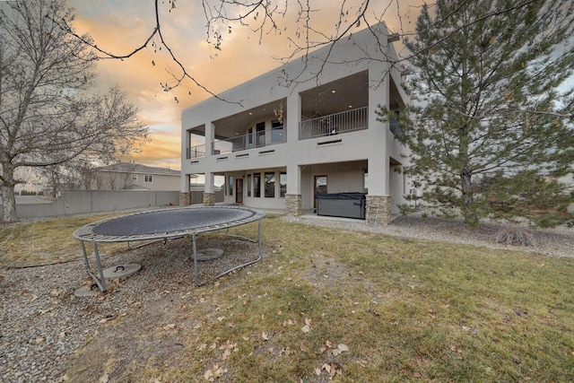 back house at dusk featuring a hot tub, a balcony, a yard, and a trampoline