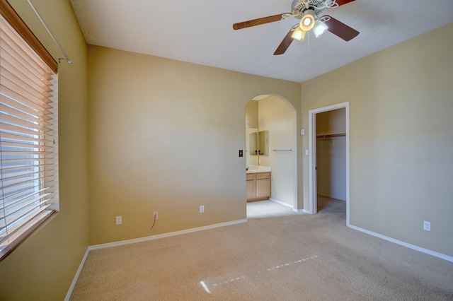 unfurnished bedroom with ensuite bath, light carpet, ceiling fan, and a closet