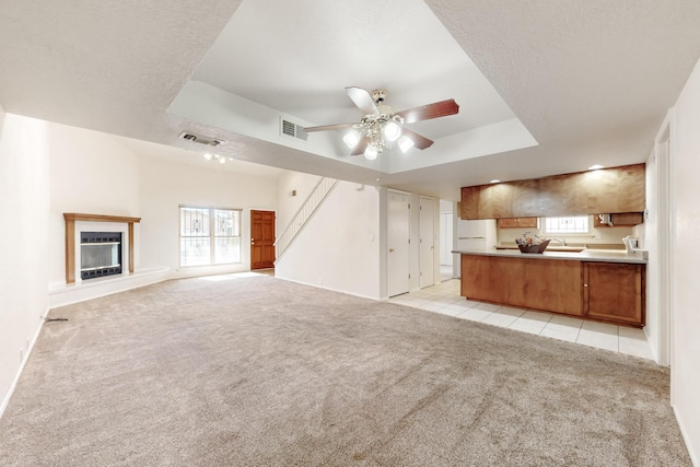 unfurnished living room with light colored carpet, a textured ceiling, ceiling fan, and a tray ceiling