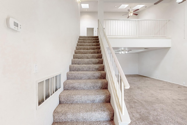 stairway featuring ceiling fan, a skylight, carpet floors, and a high ceiling