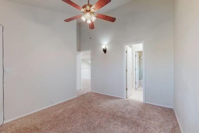 carpeted spare room with a towering ceiling and ceiling fan