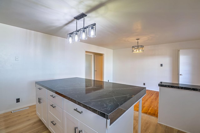 kitchen with white cabinetry, decorative light fixtures, a center island, and light hardwood / wood-style floors