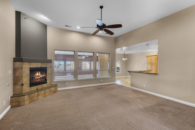 unfurnished living room with a tiled fireplace, carpet flooring, and ceiling fan