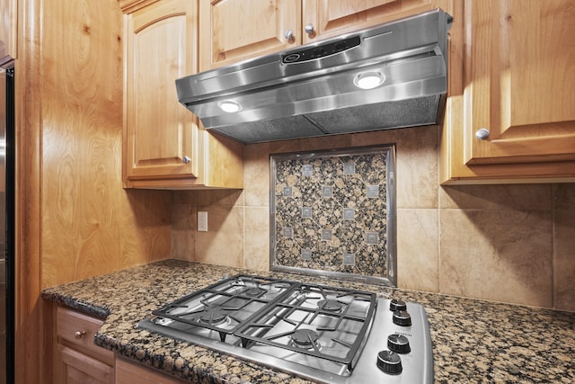 kitchen featuring stainless steel gas stovetop, decorative backsplash, and dark stone countertops