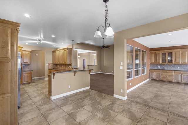 kitchen featuring decorative light fixtures, a kitchen breakfast bar, dark stone counters, decorative backsplash, and kitchen peninsula