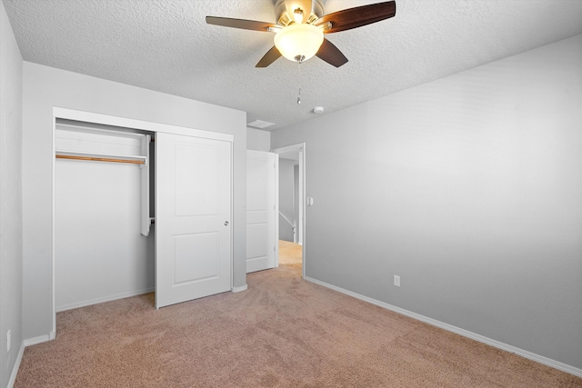 unfurnished bedroom with ceiling fan, light colored carpet, a closet, and a textured ceiling