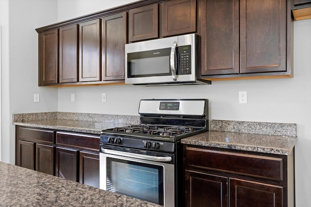 kitchen featuring appliances with stainless steel finishes, dark brown cabinets, and dark stone counters