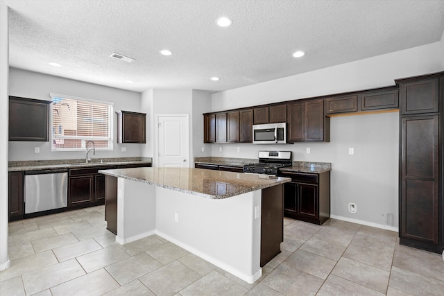 kitchen with sink, light stone counters, a textured ceiling, a kitchen island, and stainless steel appliances