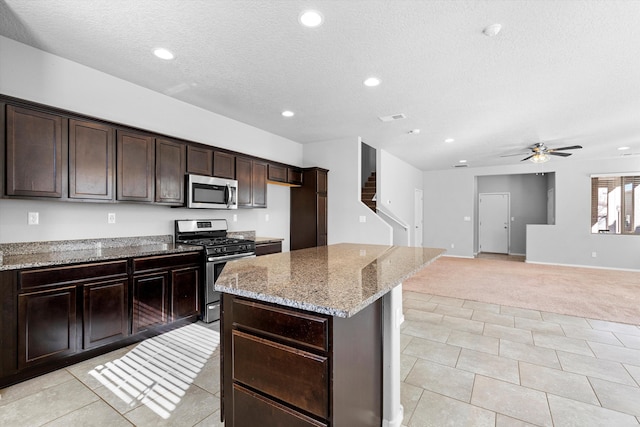 kitchen featuring light tile patterned floors, light stone counters, stainless steel appliances, dark brown cabinets, and a textured ceiling