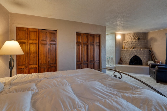 bedroom featuring a brick fireplace, two closets, and a textured ceiling