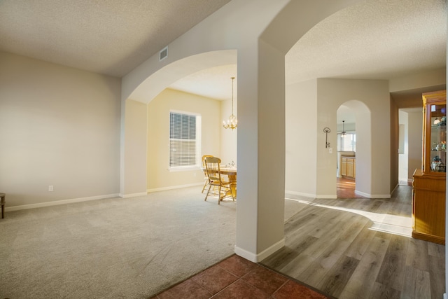 corridor featuring an inviting chandelier, plenty of natural light, carpet floors, and a textured ceiling