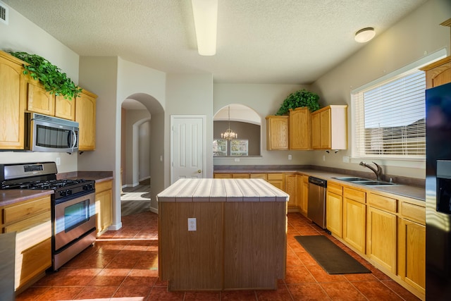 kitchen with arched walkways, appliances with stainless steel finishes, a center island, dark tile patterned floors, and a sink