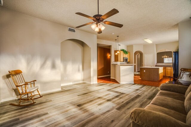 living room with visible vents, arched walkways, wood finished floors, a textured ceiling, and ceiling fan with notable chandelier