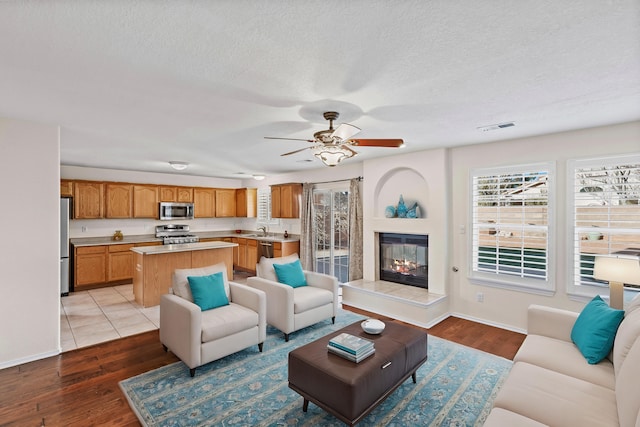 living room featuring ceiling fan, light hardwood / wood-style floors, sink, and a tile fireplace