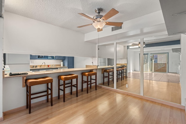 kitchen with blue cabinets, a breakfast bar area, fridge, kitchen peninsula, and light hardwood / wood-style floors