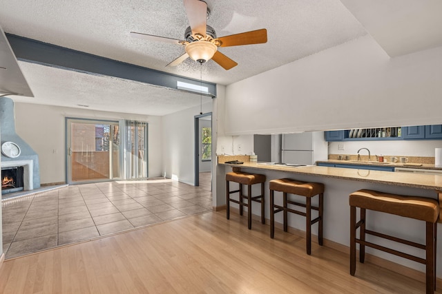 kitchen featuring blue cabinetry, a breakfast bar, sink, a large fireplace, and light hardwood / wood-style floors