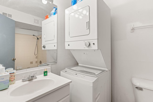 laundry area featuring stacked washer / drying machine, sink, and a textured ceiling