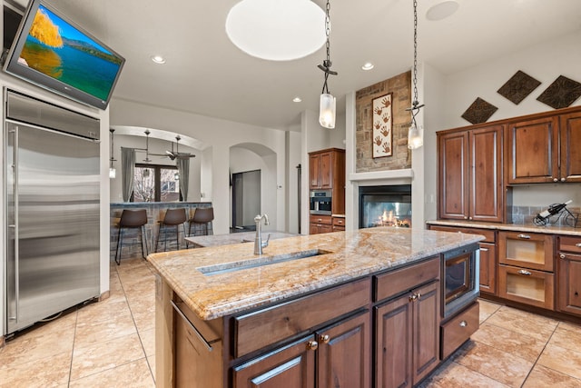 kitchen with sink, built in appliances, light tile patterned floors, an island with sink, and light stone countertops