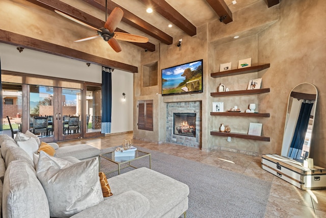 living room featuring a towering ceiling, a fireplace, ceiling fan, beam ceiling, and french doors