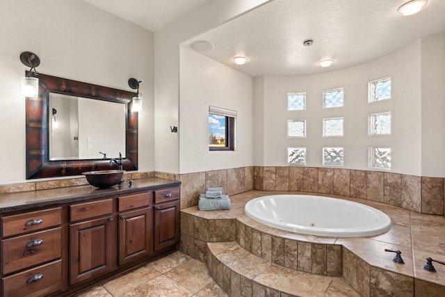 bathroom featuring a relaxing tiled tub, vanity, and a textured ceiling