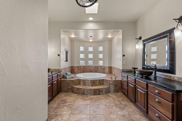 bathroom featuring vanity, a skylight, and tiled bath