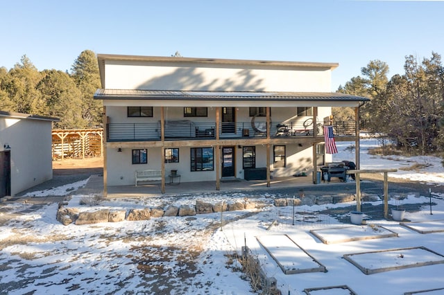 snow covered back of property featuring metal roof, a balcony, a standing seam roof, and a patio area