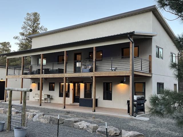 back of property featuring a balcony, a patio area, and stucco siding