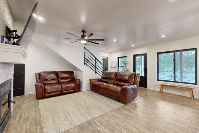 living area featuring stairway, recessed lighting, a stone fireplace, and light wood-style floors