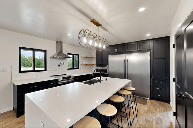 450 Juan Tomas Rd, Tijeras, NM 87059 - kitchen with stainless steel appliances, wall chimney exhaust hood, dark cabinets, decorative backsplash, and light wood-style floors