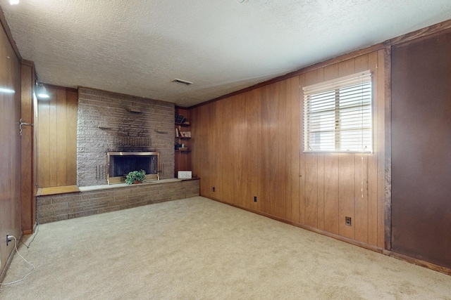 unfurnished living room with a fireplace, wooden walls, light colored carpet, and a textured ceiling