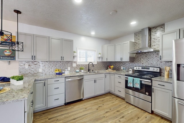 kitchen featuring sink, decorative light fixtures, a textured ceiling, stainless steel appliances, and wall chimney range hood