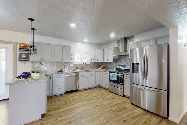 kitchen with sink, appliances with stainless steel finishes, a textured ceiling, decorative light fixtures, and wall chimney exhaust hood