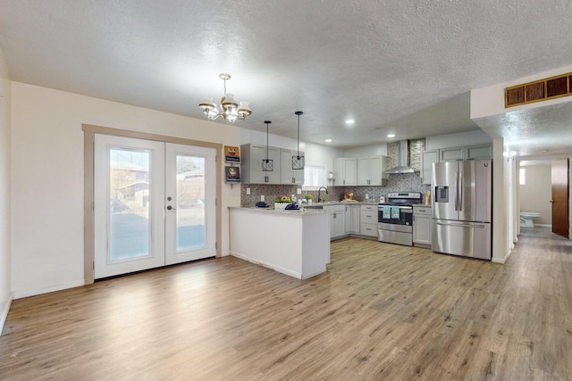 kitchen featuring appliances with stainless steel finishes, pendant lighting, sink, backsplash, and wall chimney range hood