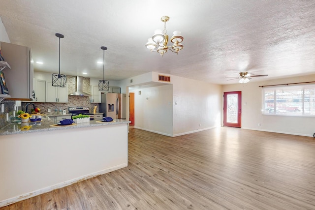 kitchen featuring wall chimney range hood, appliances with stainless steel finishes, tasteful backsplash, decorative light fixtures, and kitchen peninsula