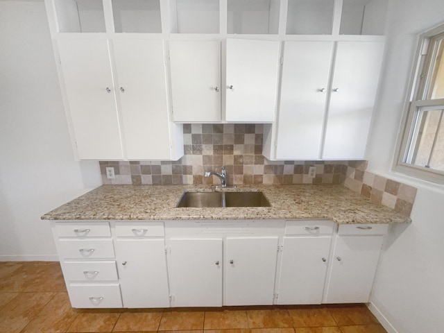 kitchen featuring light stone counters, a sink, and white cabinets