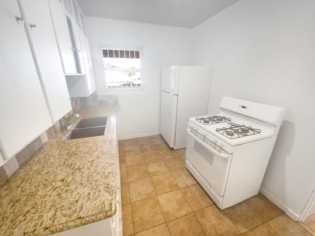 kitchen featuring white appliances, white cabinets, a sink, and baseboards