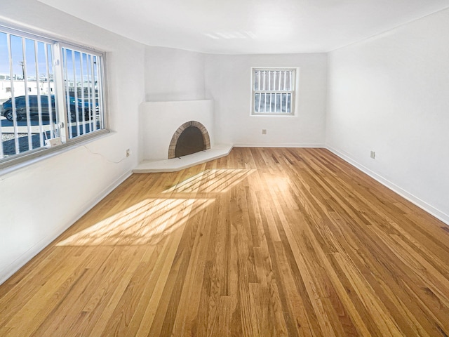 unfurnished living room with a healthy amount of sunlight, a fireplace with raised hearth, baseboards, and wood finished floors