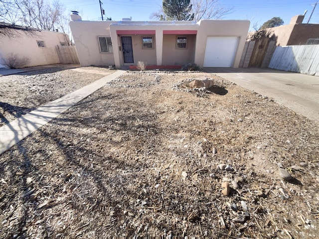 pueblo-style home featuring driveway, an attached garage, fence, and stucco siding