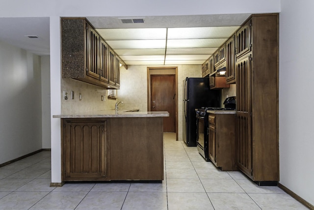 kitchen with light tile patterned flooring, dark brown cabinetry, kitchen peninsula, and gas stove