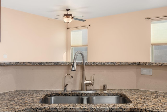 kitchen featuring ceiling fan, sink, and dark stone countertops