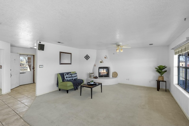 sitting room featuring ceiling fan, a fireplace, light carpet, and a textured ceiling