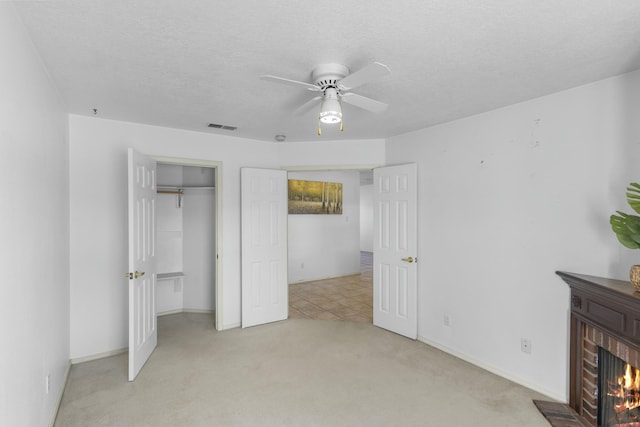 unfurnished bedroom with ceiling fan, a textured ceiling, a brick fireplace, light colored carpet, and a closet