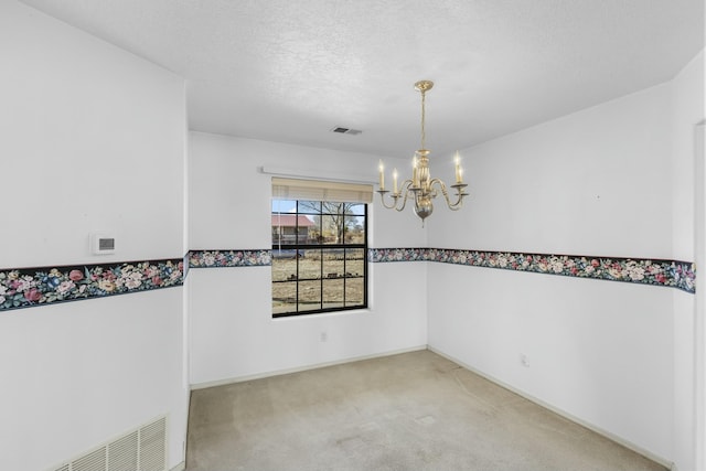 carpeted empty room featuring a textured ceiling and an inviting chandelier